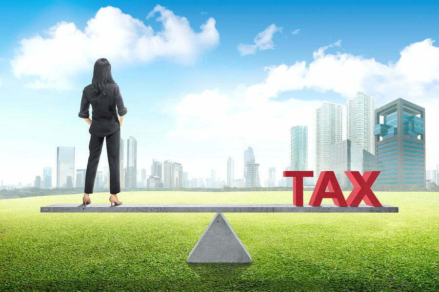 Graphic image of a woman on a balance beam with the word TAX on the other end and a cityscape in the background