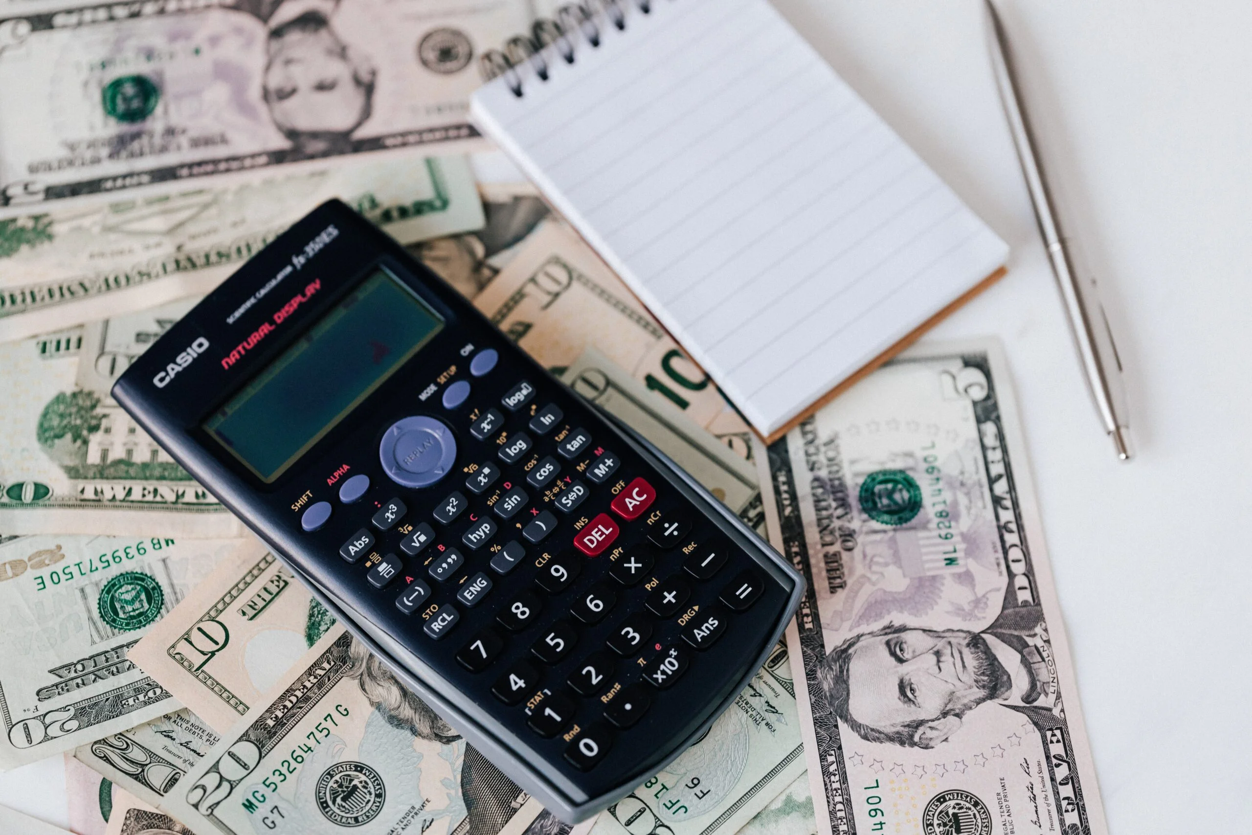 Image of cash on a desk with a notepad, pen, and calculator